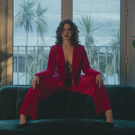 Katrina Fairhurst, a writer for adult brands, sits in front of a window wearing a striking red suit